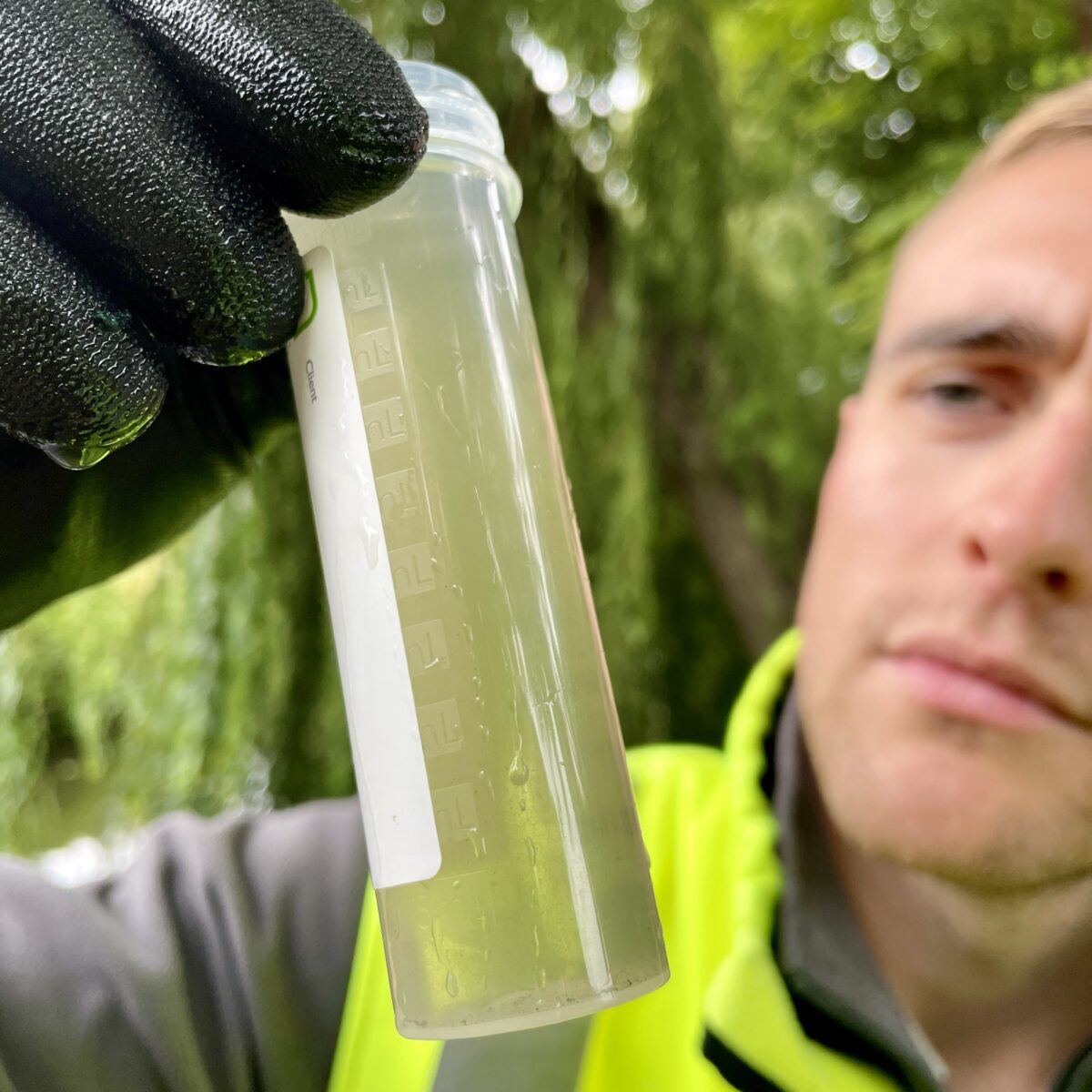 Man in high vis jacket and gloves holding tube of polluted water