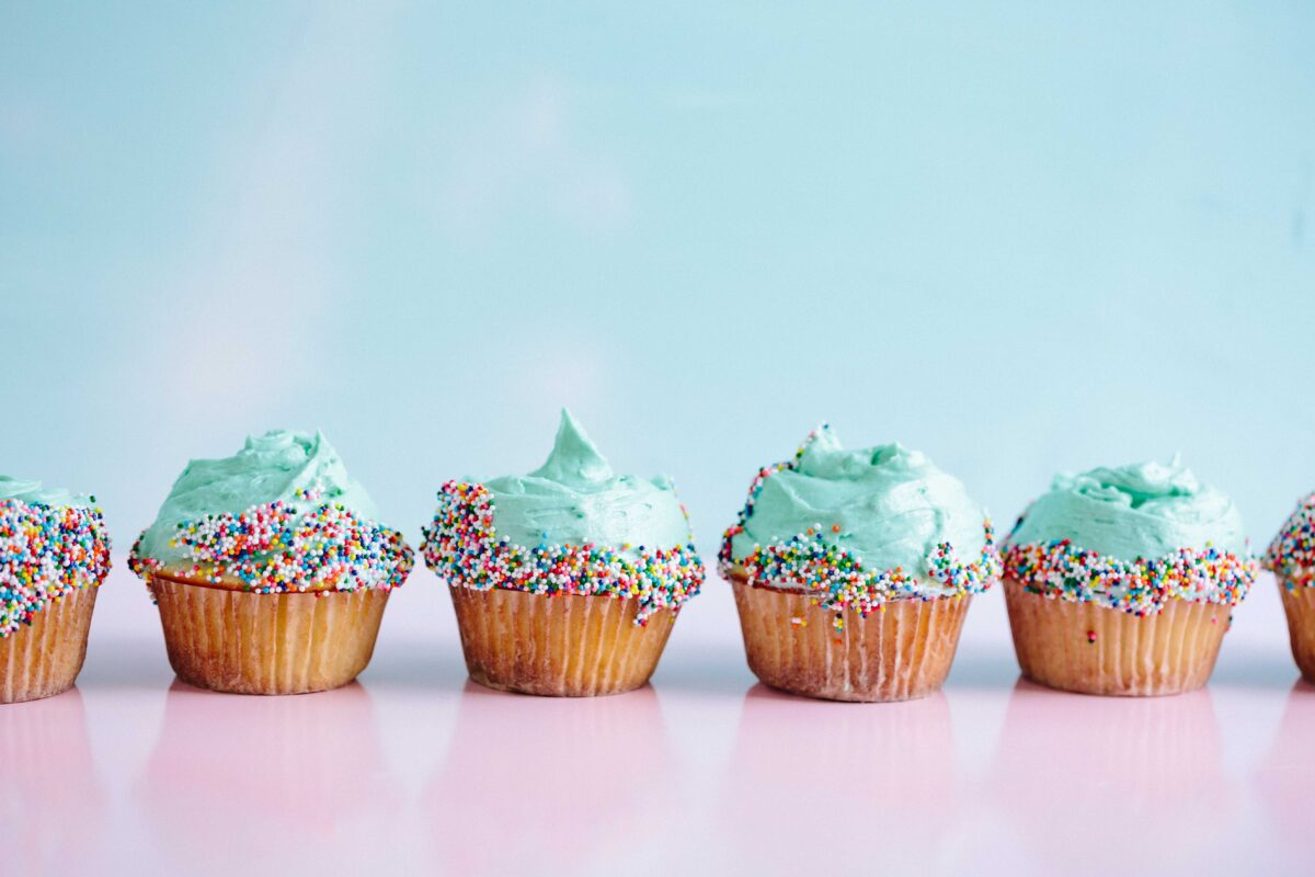 Six cupcakes in a row with blue icing and sprinkles