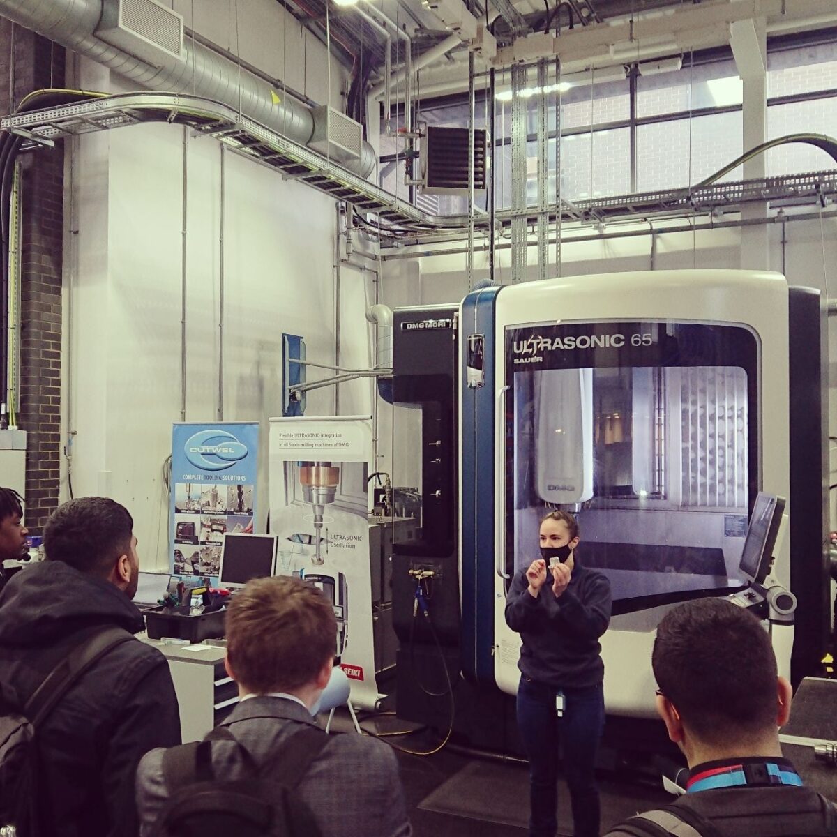 Bethany standing in front of a design machine talking to a group of people