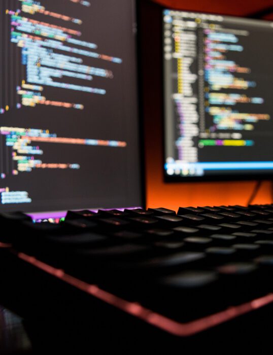 Keyboard and two screens with code on them